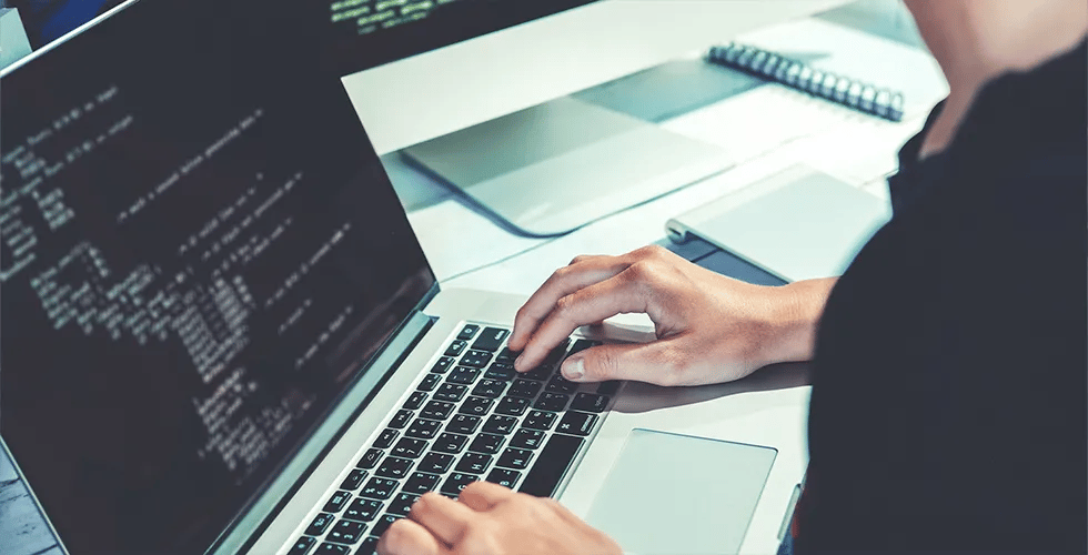 An IT expert sits at the laptop programming the code of the API.