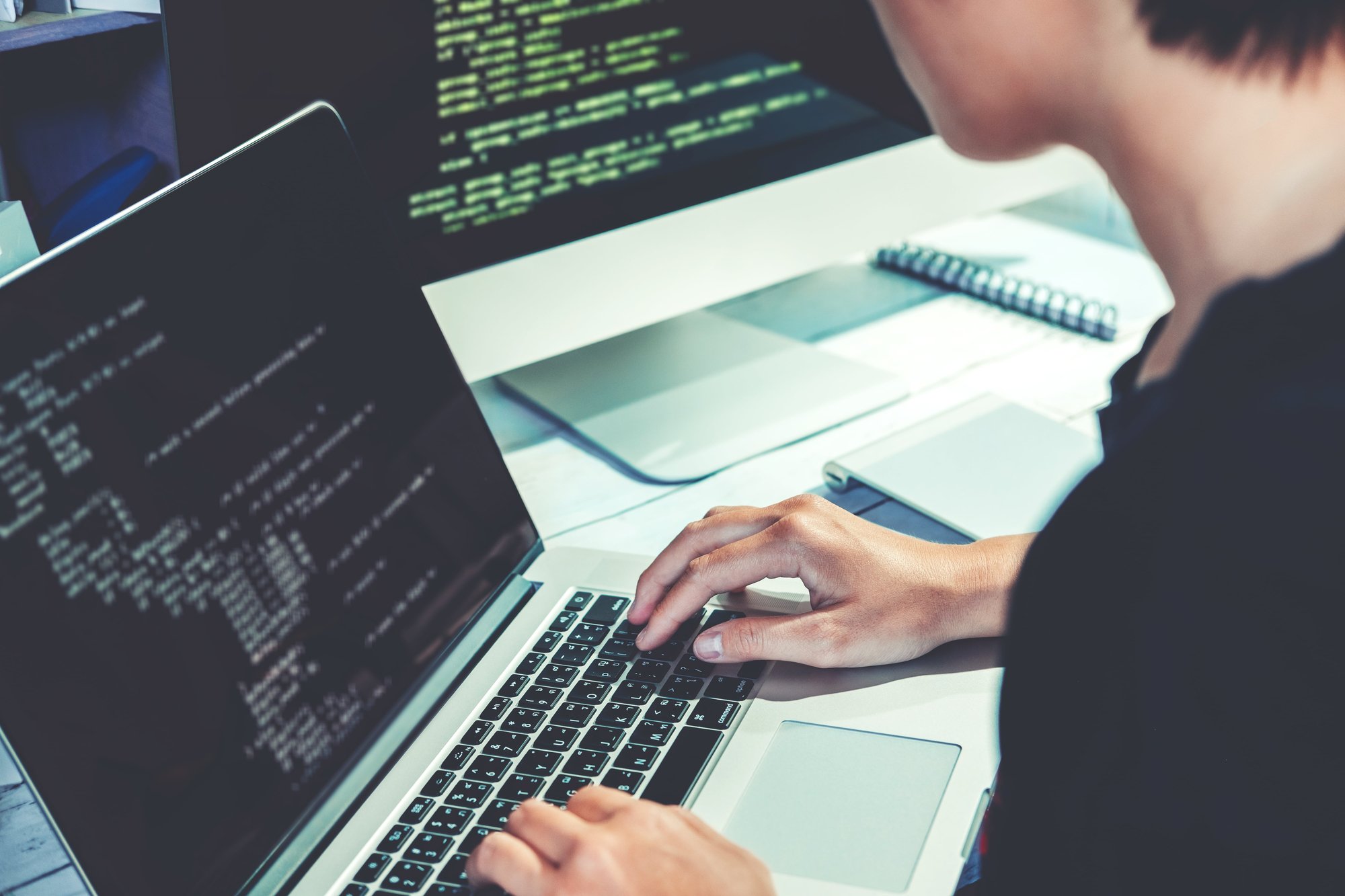 Person schreibt Code an zwei Rechnern