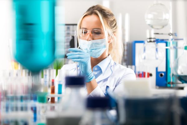 Ärztin mit Pipette umgeben von Reagenzgläsern-600x400
