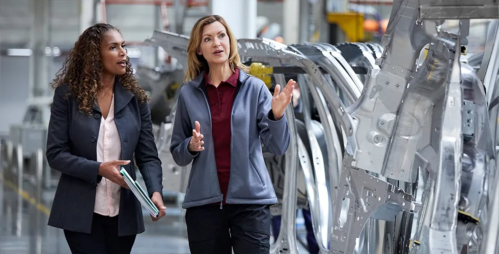 Zwei Ingenieurinnen sprechen über die Produktion von Autoteilen. Eine hält die übersetzen Produktionsunterlagen in der Hand.
