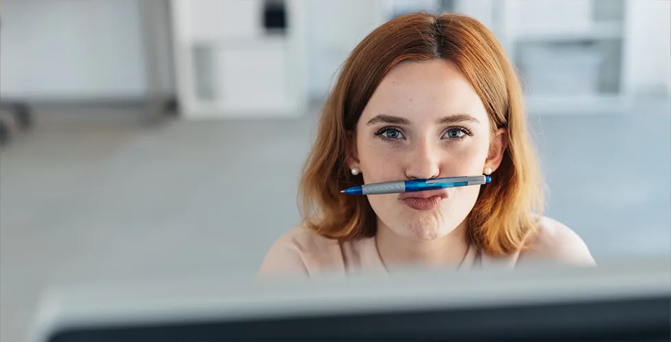 A young woman needs help translating a contract and pinches a pen between her lips and nose.