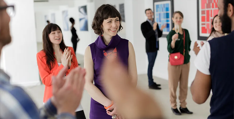 Eine Malerin steht in ihrem Atelier und bekommt Applaus für ihre internationale Ausstellung.