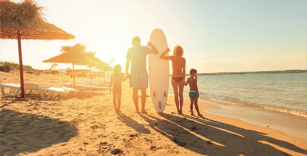 Eine Familie mit zwei Kindern schaut am Strand in den Sonnenuntergang.