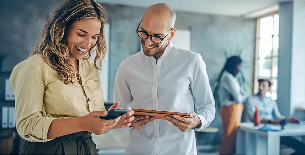Eine junge Frau und ein junger Mann vergleichen Übersetzungskosten auf ihrem Smartphone und seinem Tablet.