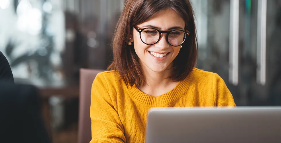 Eine junge Frau schaut auf einen Laptop und freut sich über den tolingo Webshop