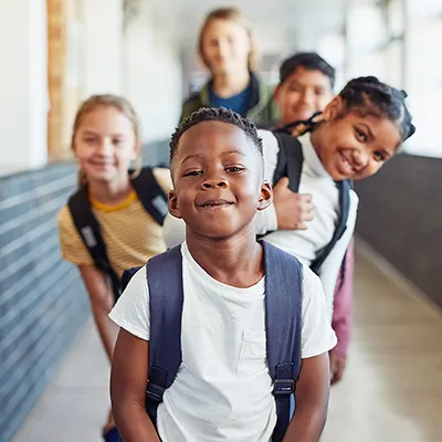 A group of children from different cultures stand in the school corridor and smile at the camera.